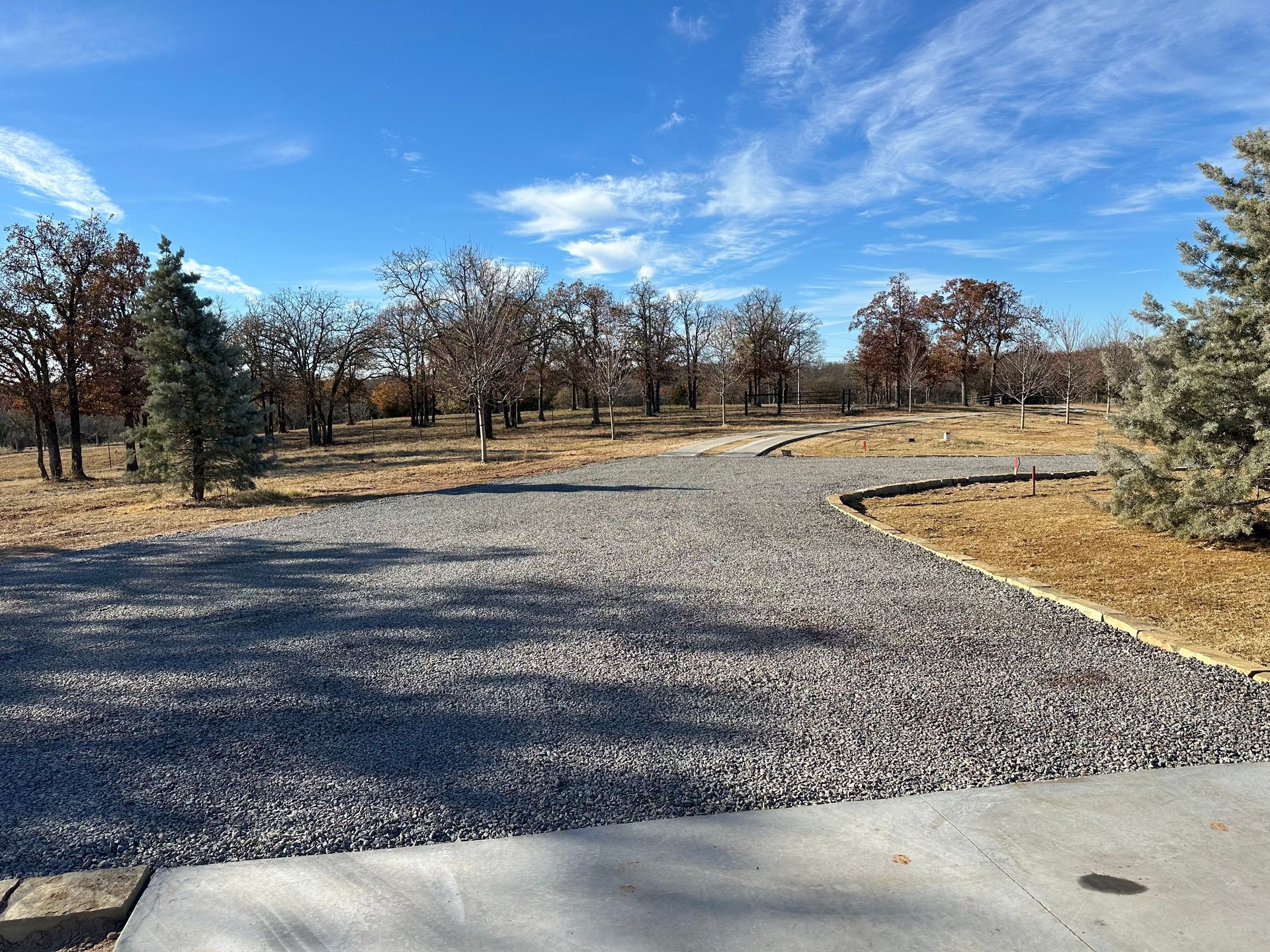 A gravel road going through a field with trees on both sides.