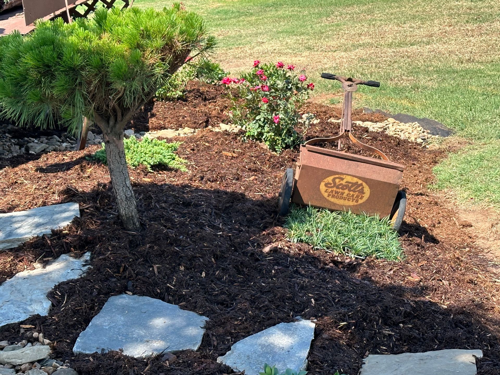 A wagon is sitting in the middle of a garden next to a tree.