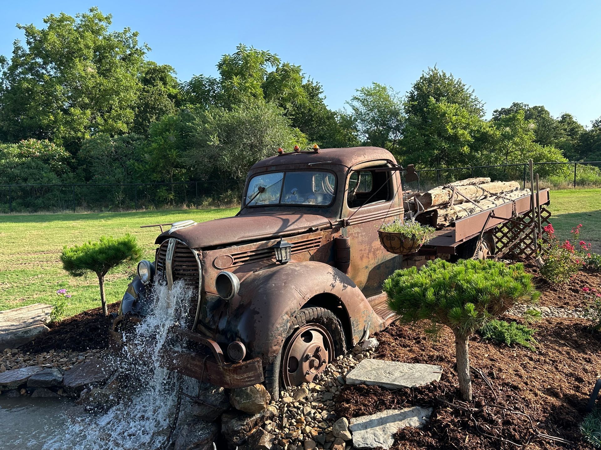 An old rusty truck is parked in a field next to a fountain.