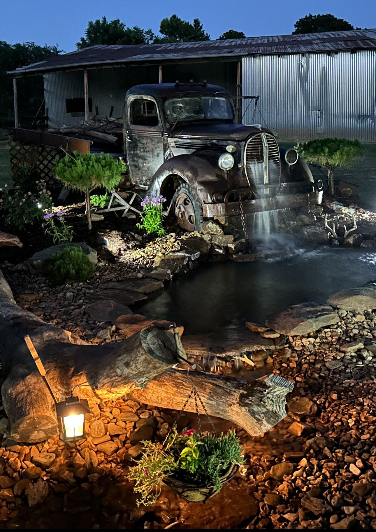 An old truck is parked next to a waterfall in front of a house.