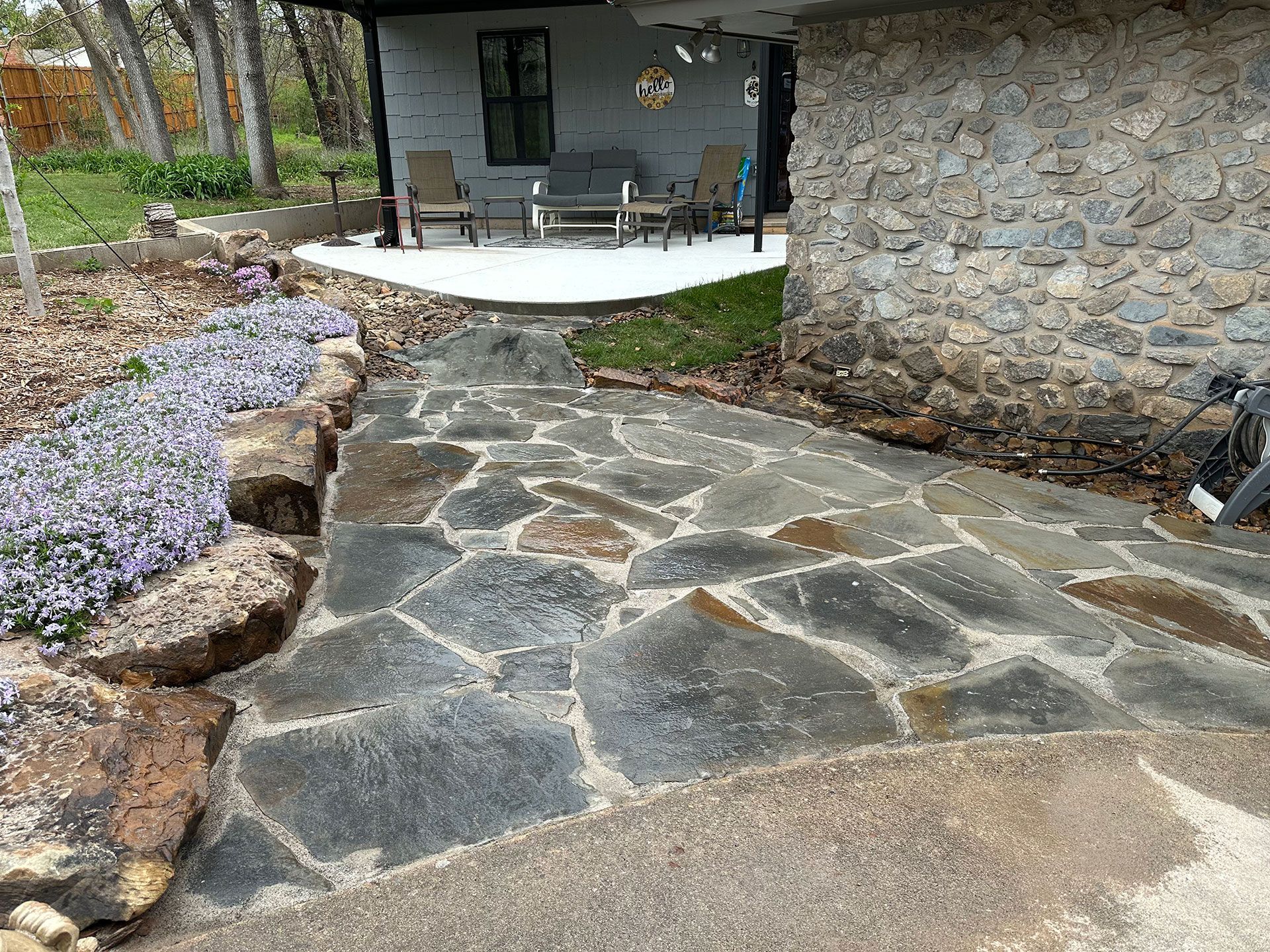 a stone walkway leading to a porch with chairs and a table
