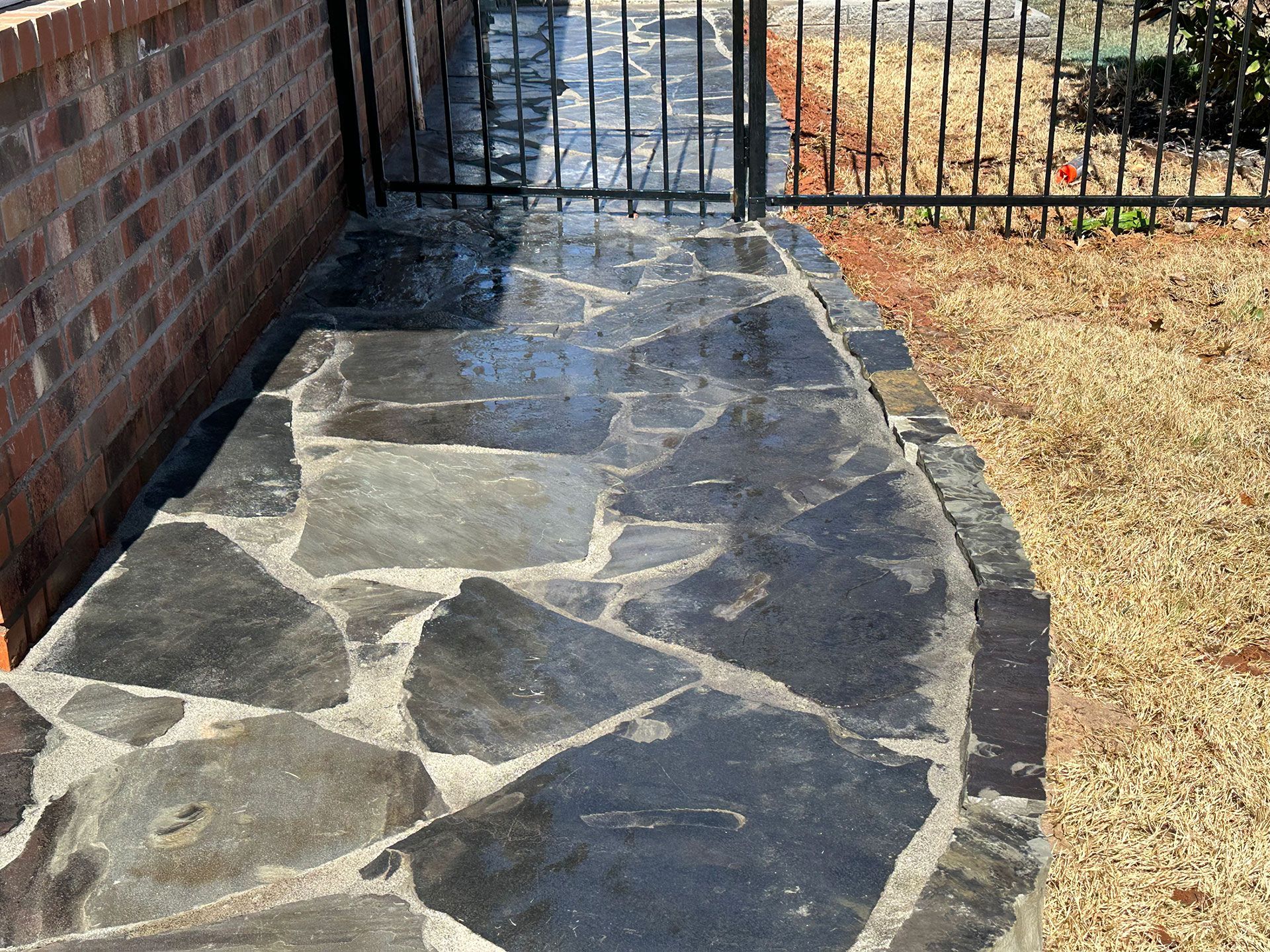 a stone walkway leading to a fence with a brick wall in the background