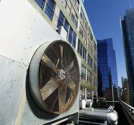Large industrial fan on rooftop, old building, blue skyscrapers in background. Bright sunlight.