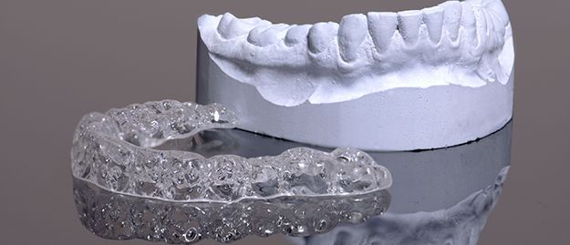 A model of a person 's teeth and a clear retainer.