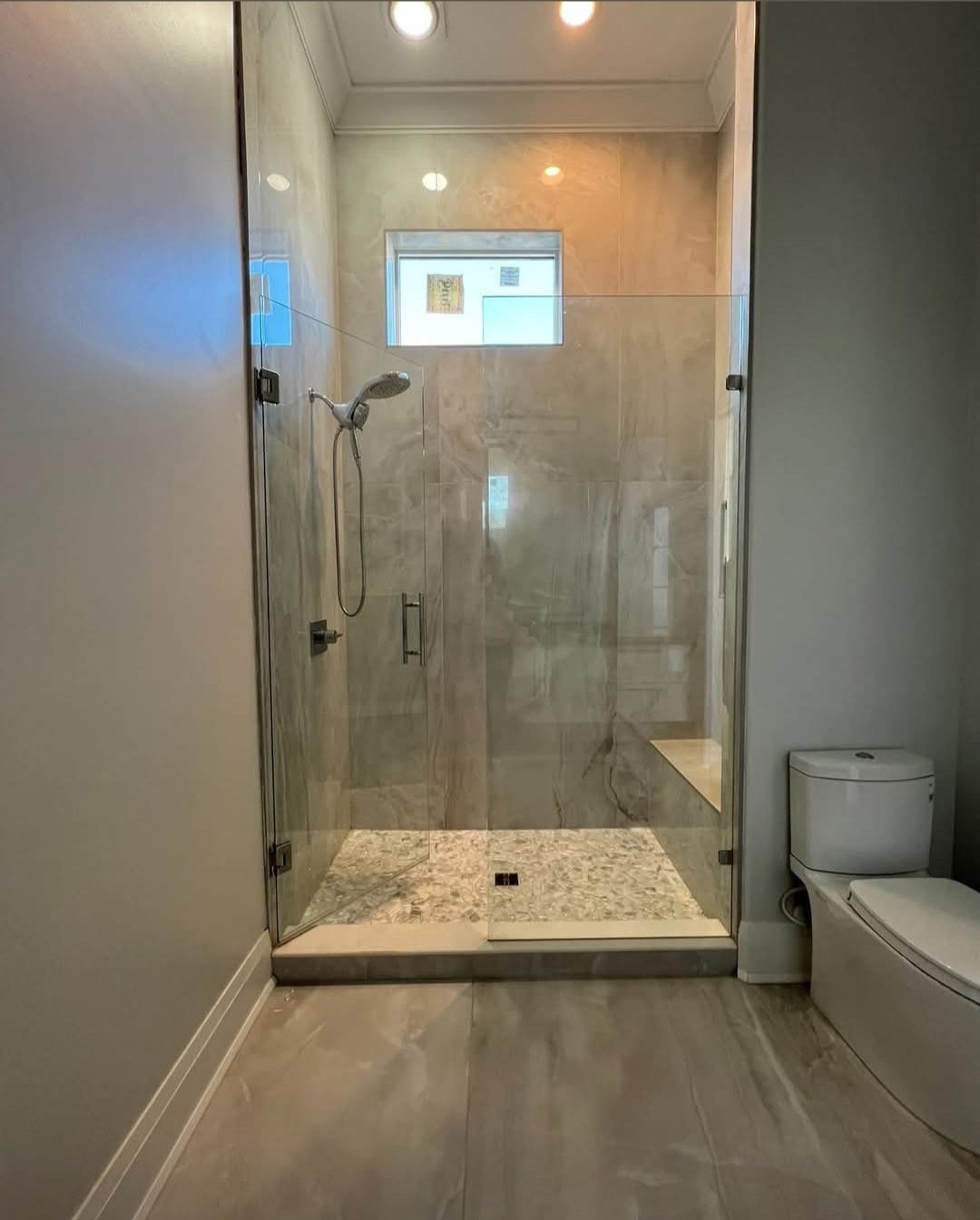 A walk-in shower with glass doors, pebble floor, built-in seat, and a toilet in a modern bathroom