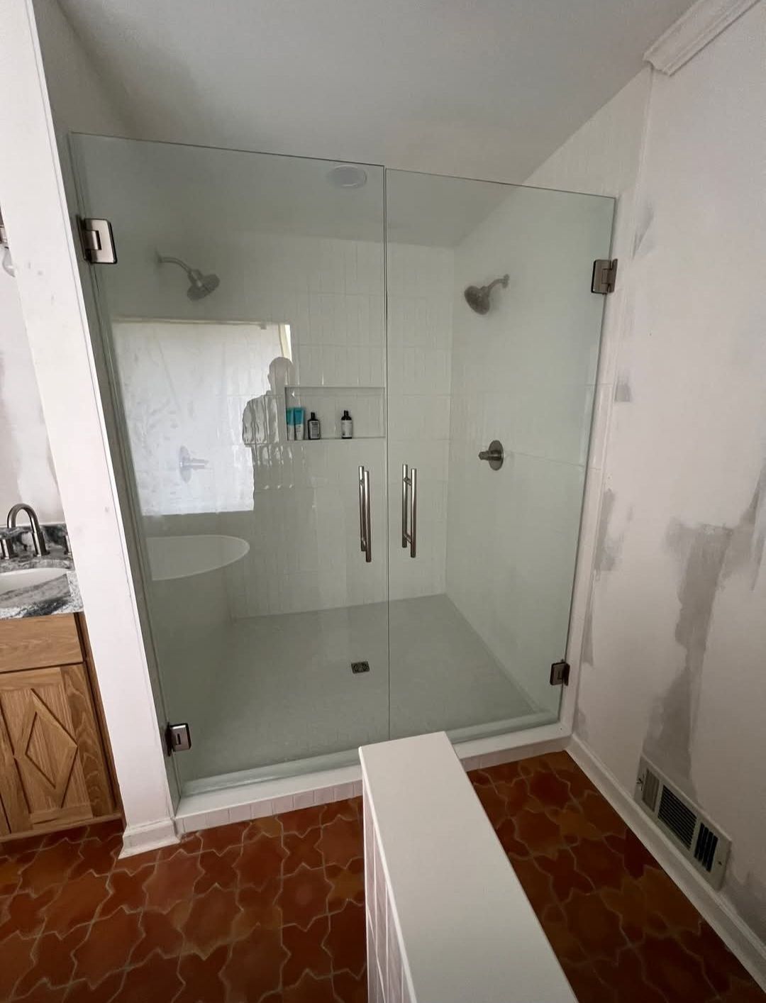 Glass shower enclosure in a bathroom with white walls and wood cabinets