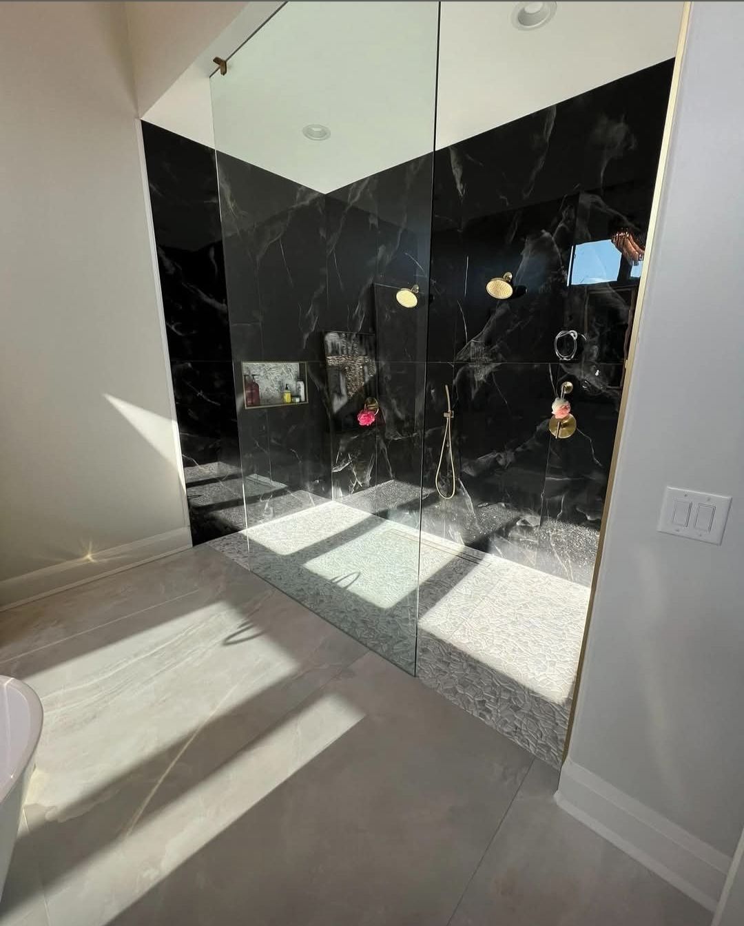 Modern bathroom with black tiled shower, glass door, and light gray floor