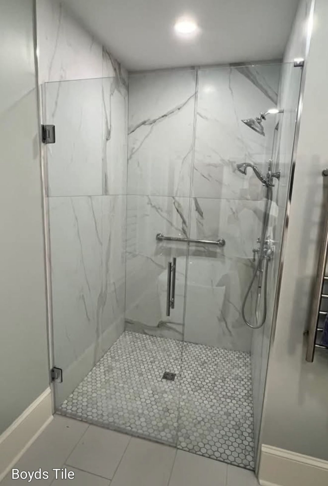 Marble-tiled shower with a glass door and pebble floor