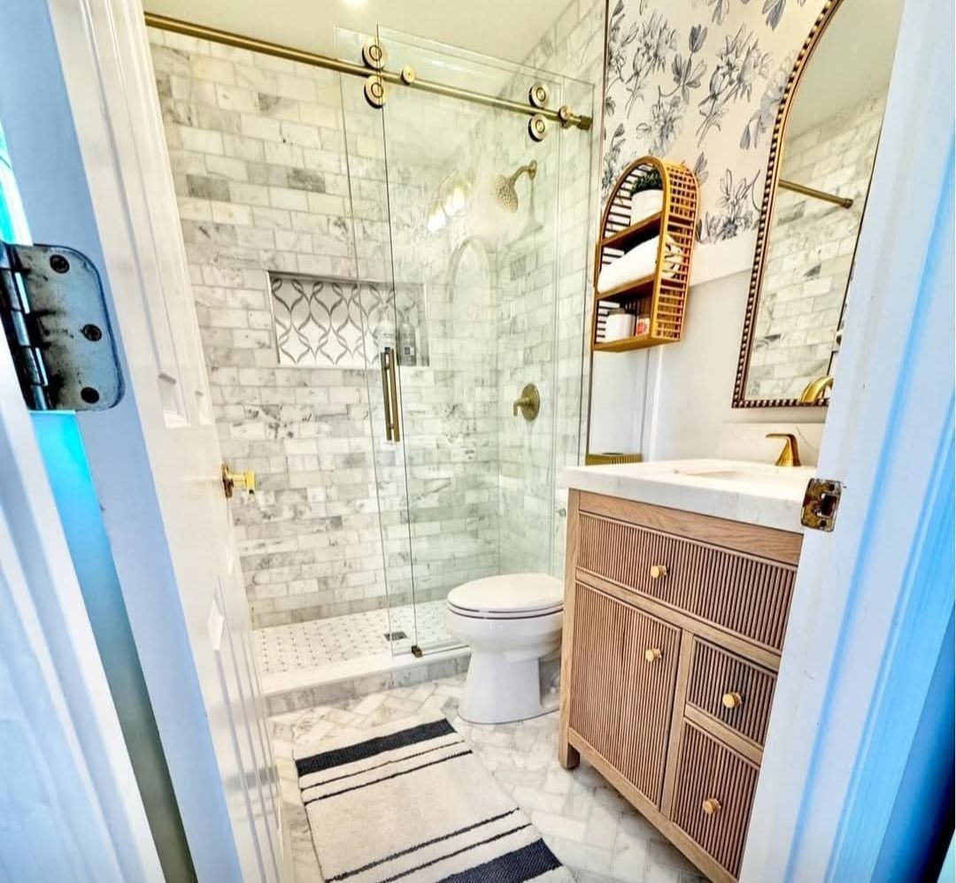 Small bathroom with marble shower, floral wallpaper, and wooden vanity
