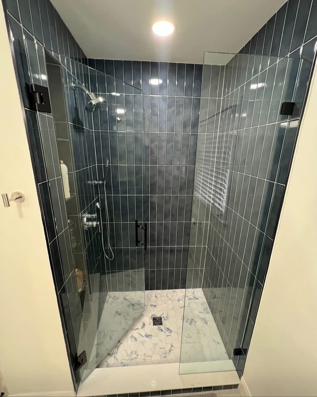 Modern shower with blue-tiled walls, glass doors, and marble floor