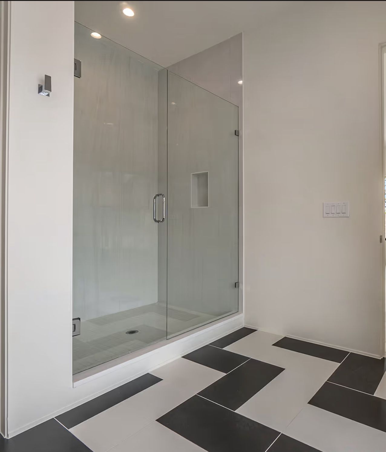 Glass shower enclosure in a modern bathroom with geometric black and white tile flooring