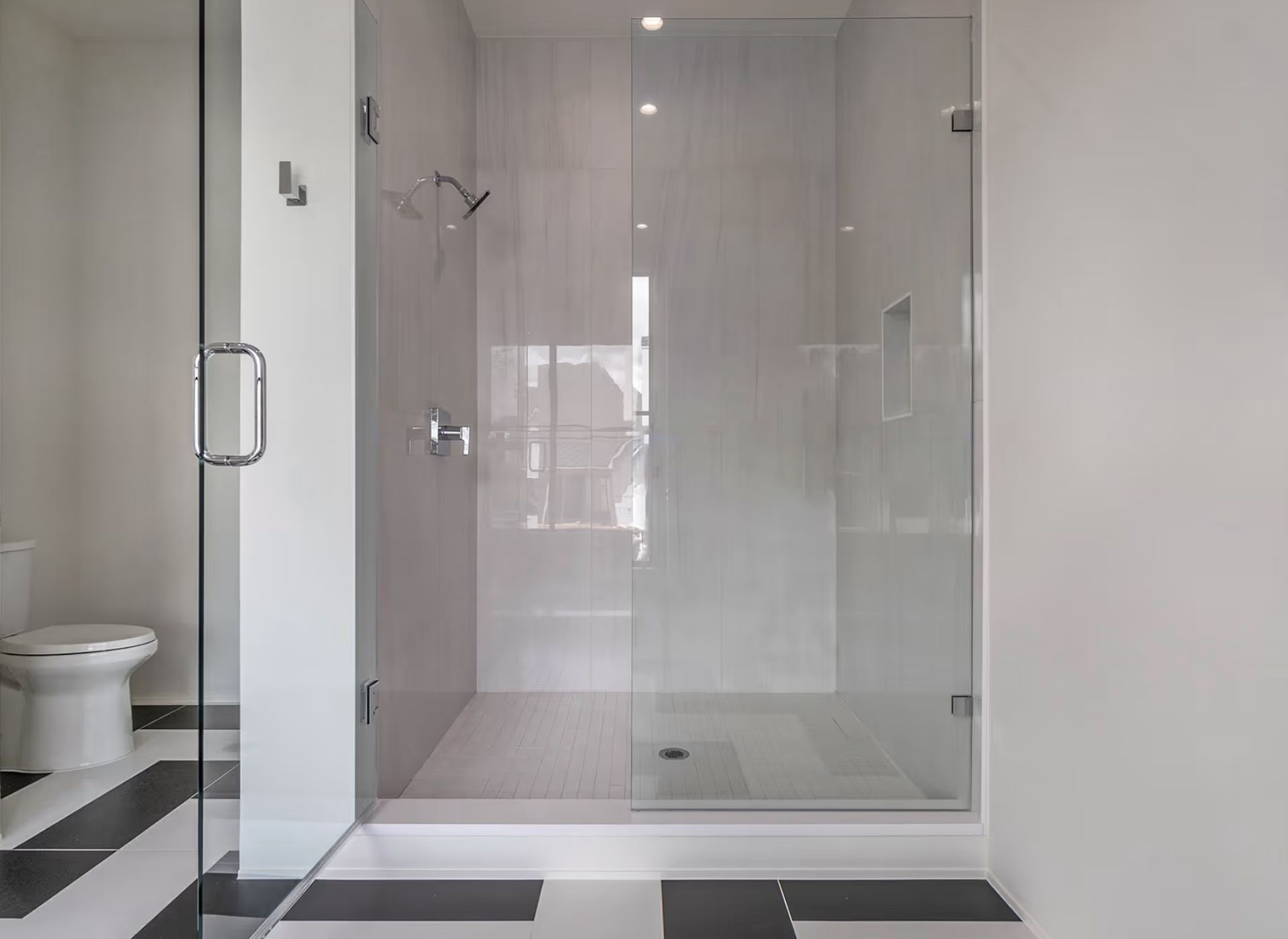 Modern glass shower in a bathroom with white walls and black and white floor tiles
