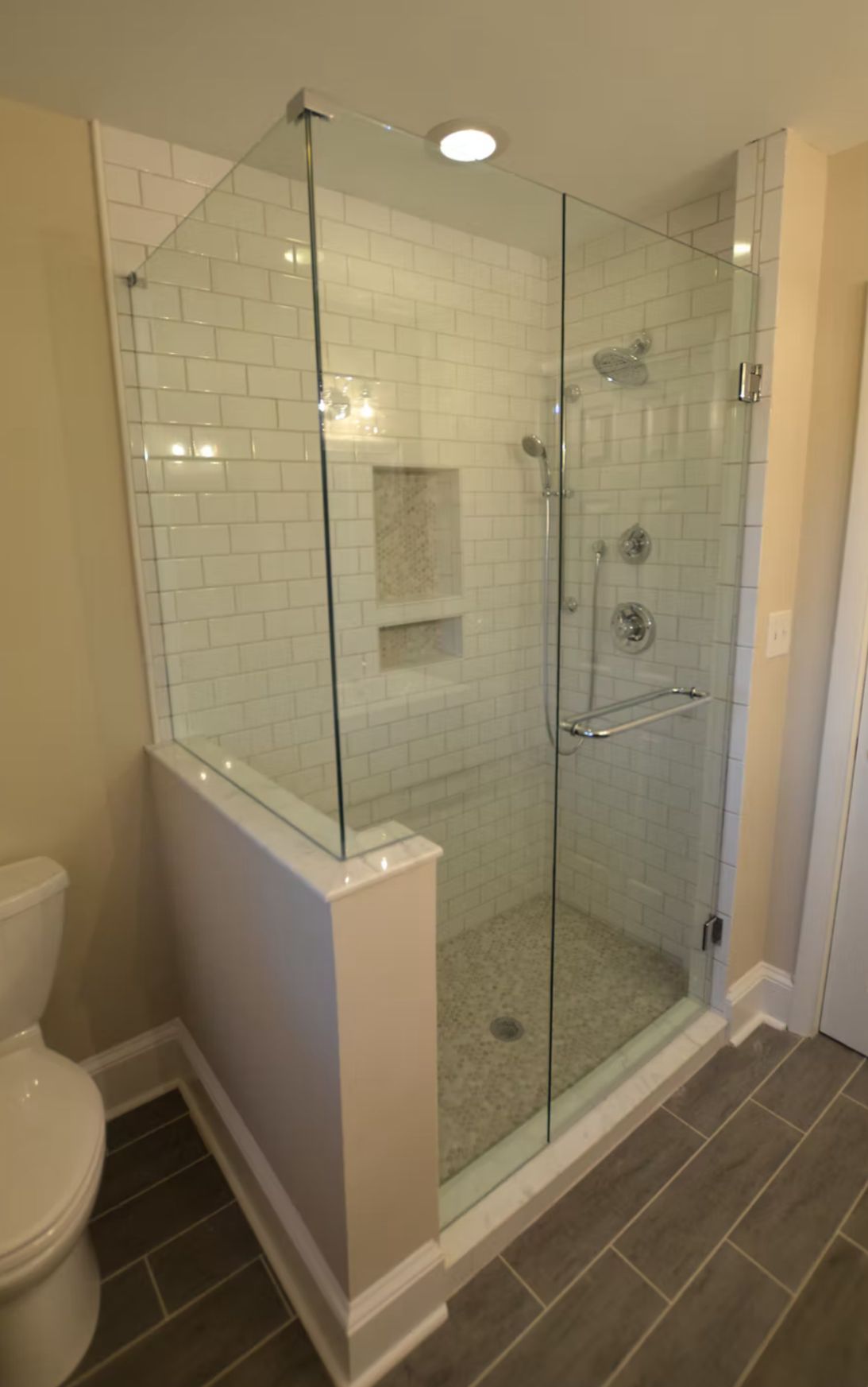 Modern glass shower with white subway tile, a recessed shelf, and a pebble floor