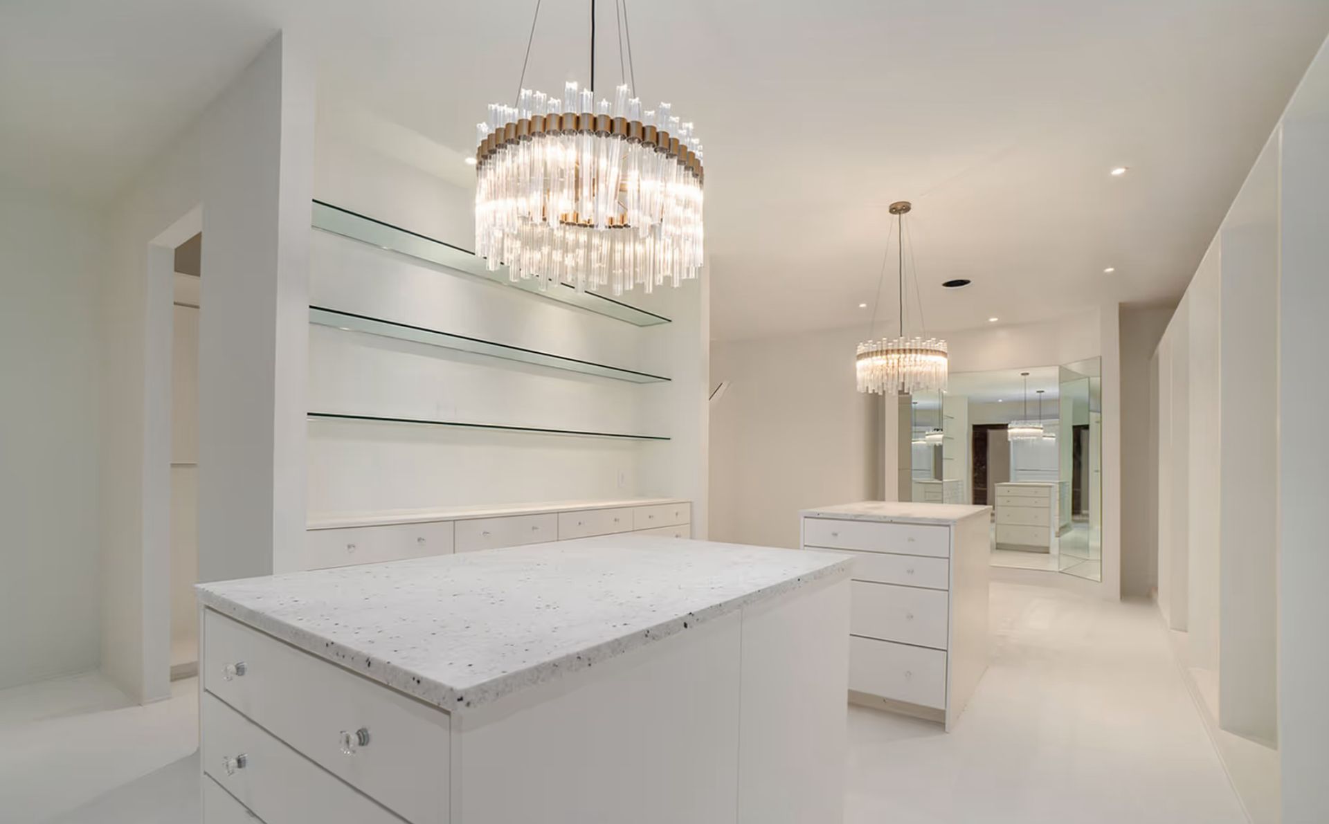 White modern walk-in closet with crystal chandeliers, shelves, and center islands