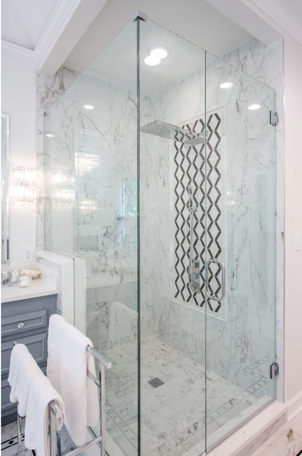 Glass-walled shower with white marble tiles and a decorative dark tile accent