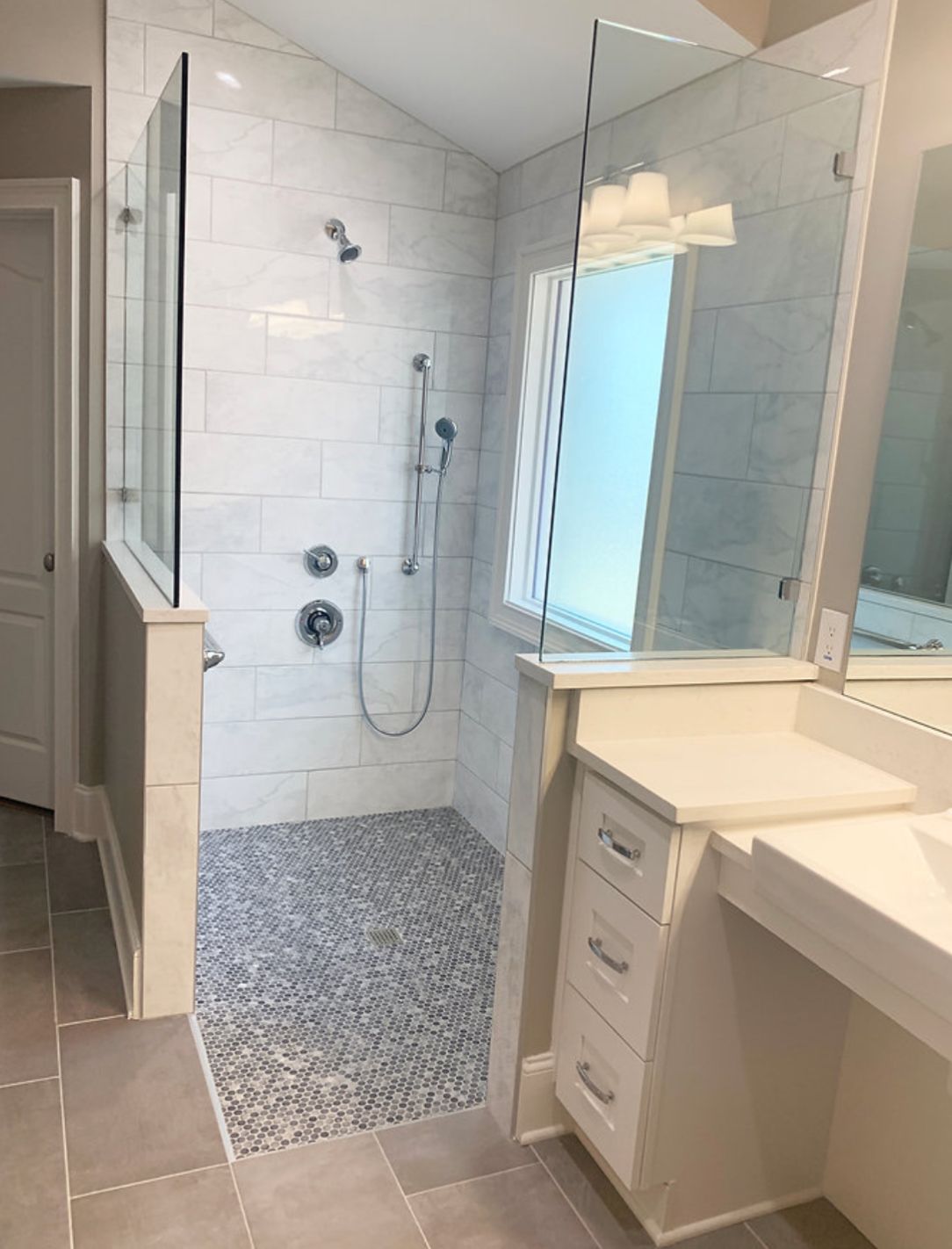 Walk-in shower with pebble floor, white subway tile walls, and glass enclosure; next to a vanity