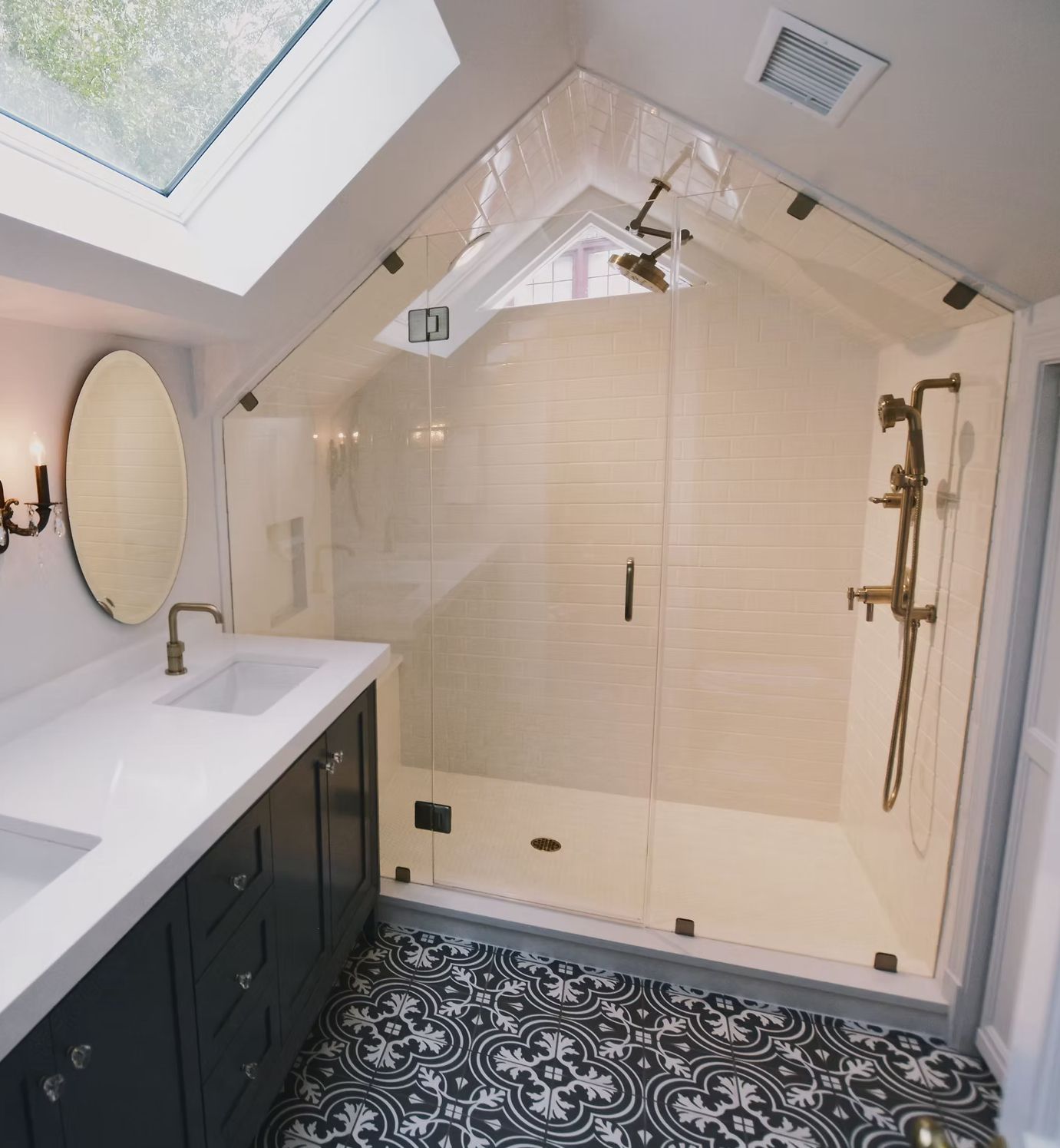 Bathroom with white walls, patterned floor, glass shower, vanity with two sinks, and skylight