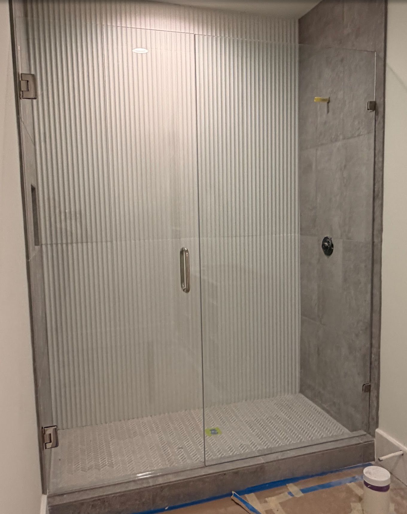 Shower enclosure with vertically-ribbed glass doors and gray tiled walls and floor