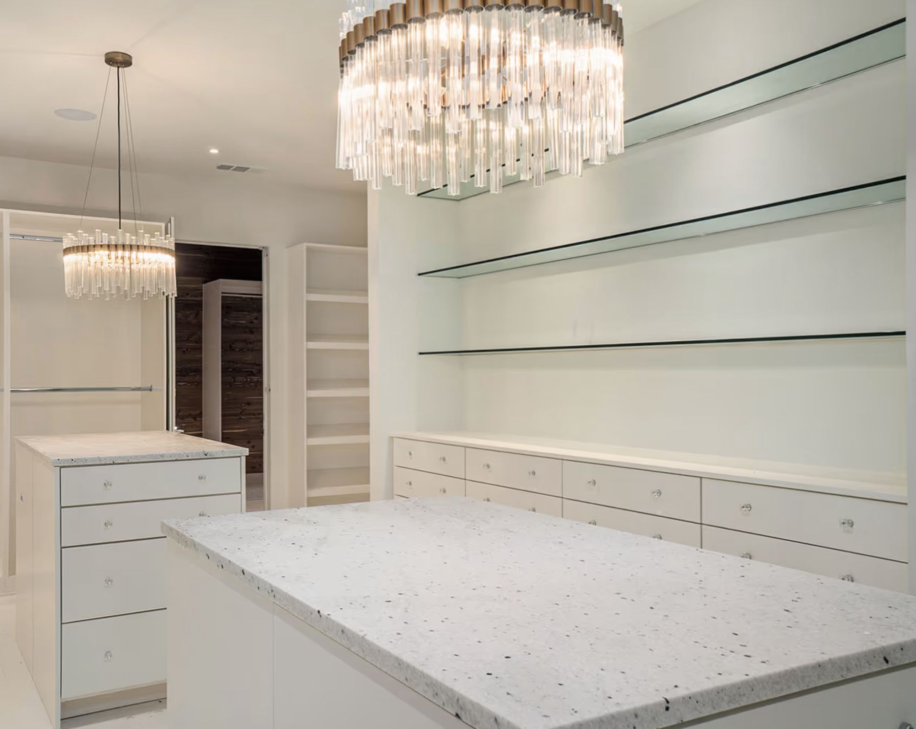 Modern white walk-in closet with crystal chandeliers, shelves, and a large central island