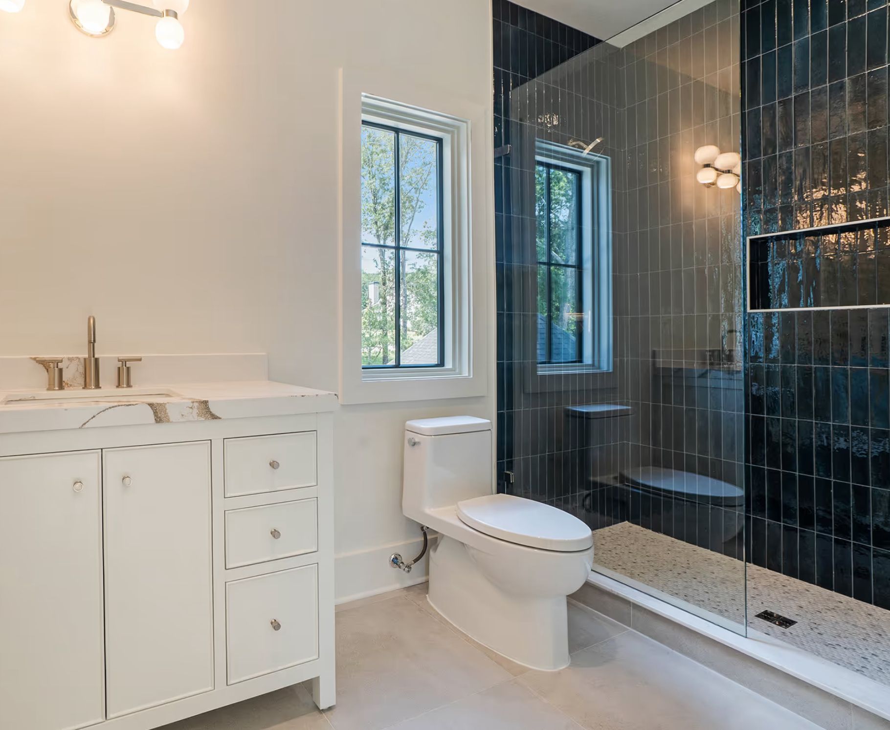 Modern bathroom with white vanity, toilet, and black-tiled shower with glass door