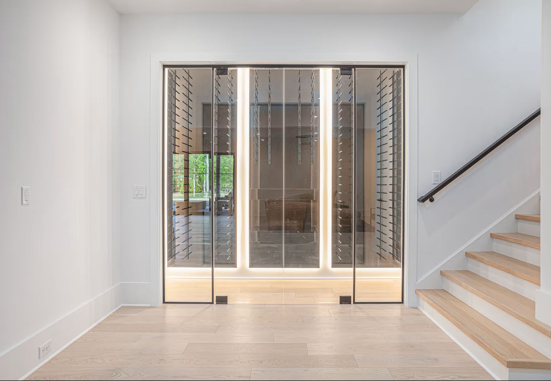 Modern wine cellar with glass doors, built-in bottle racks, and ambient lighting, next to a staircase