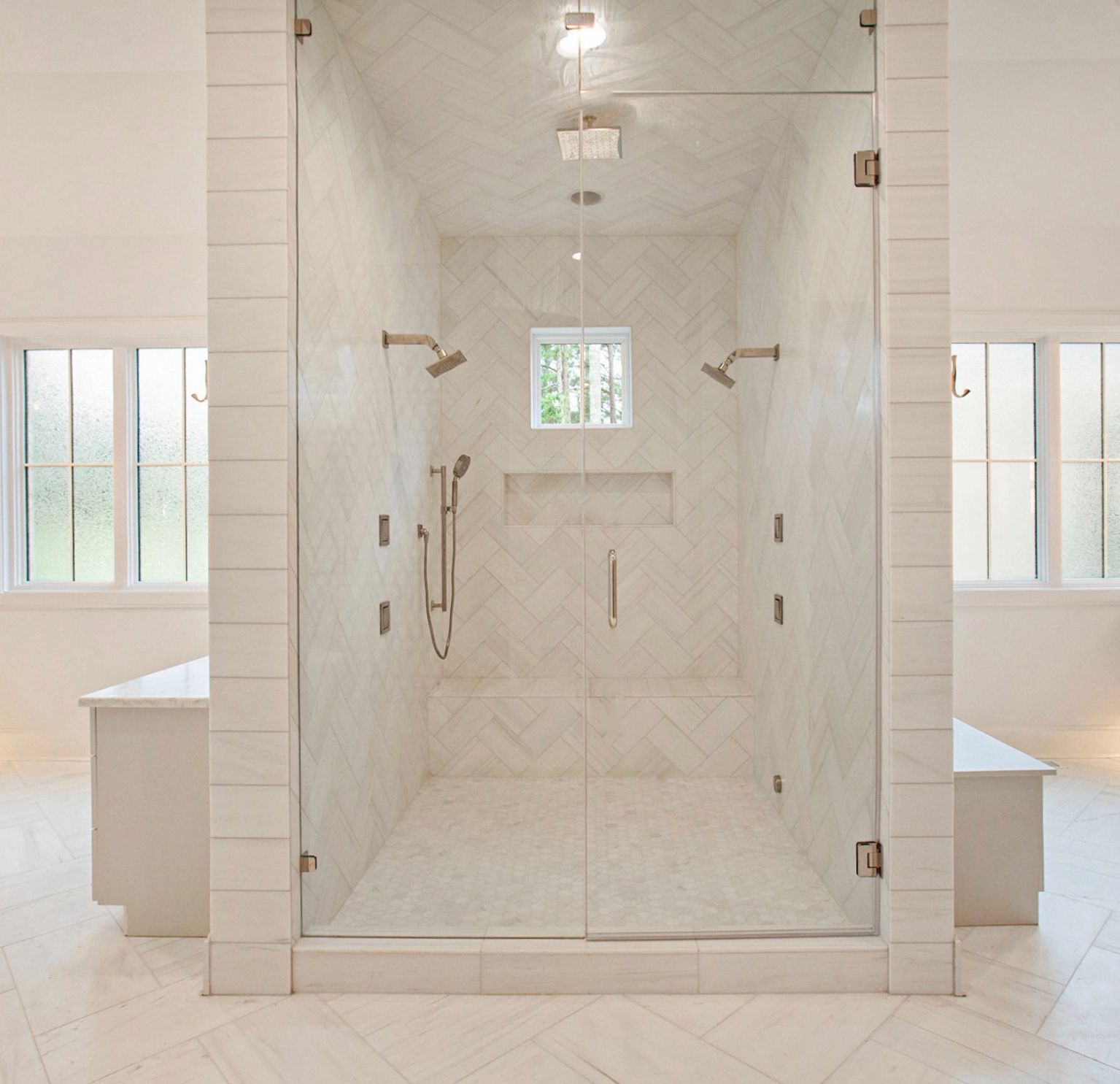 Spacious marble shower with glass doors, multiple shower heads, and built-in bench