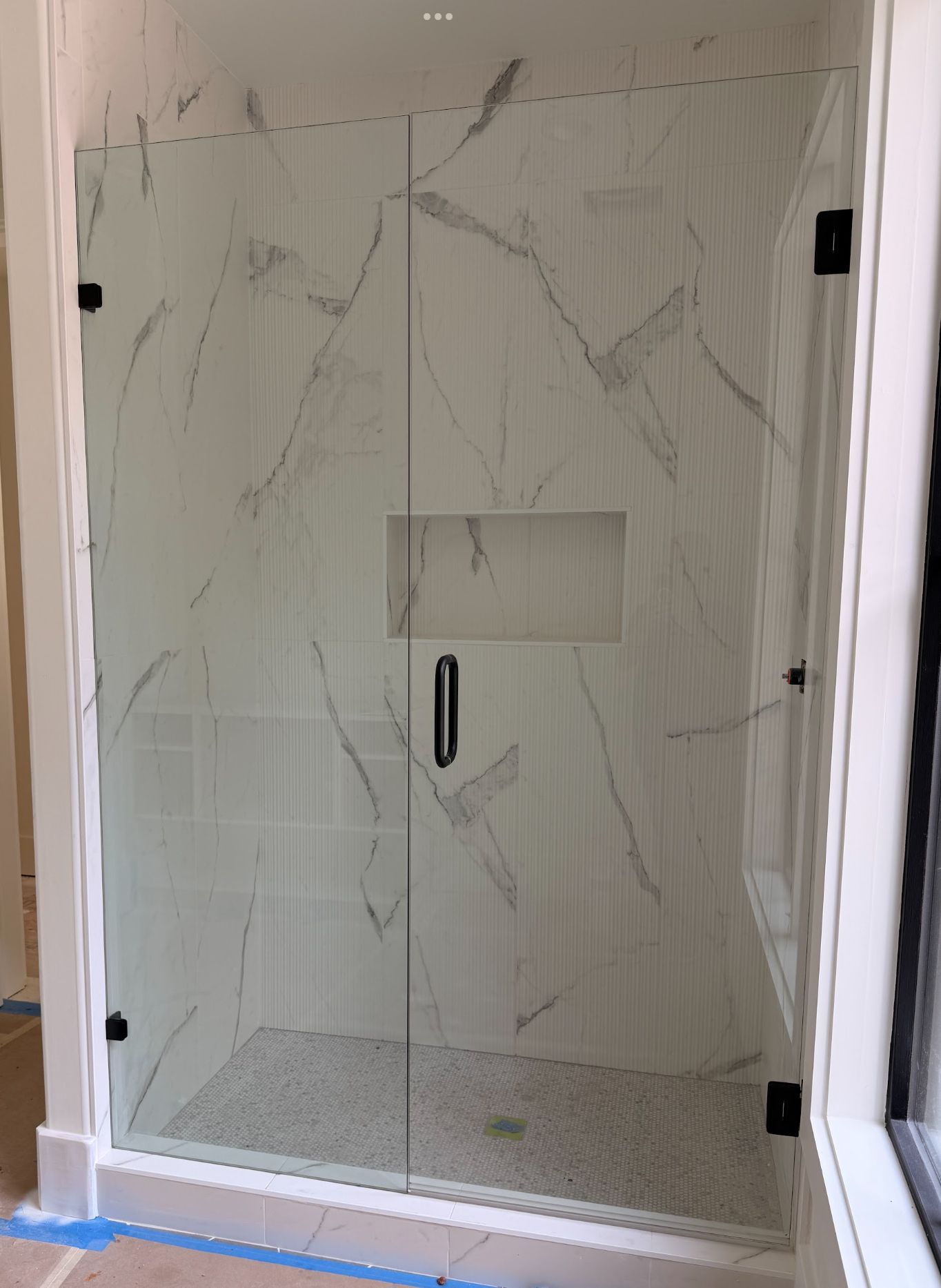 Glass shower enclosure with black hardware, marble-patterned tile, and a recessed niche