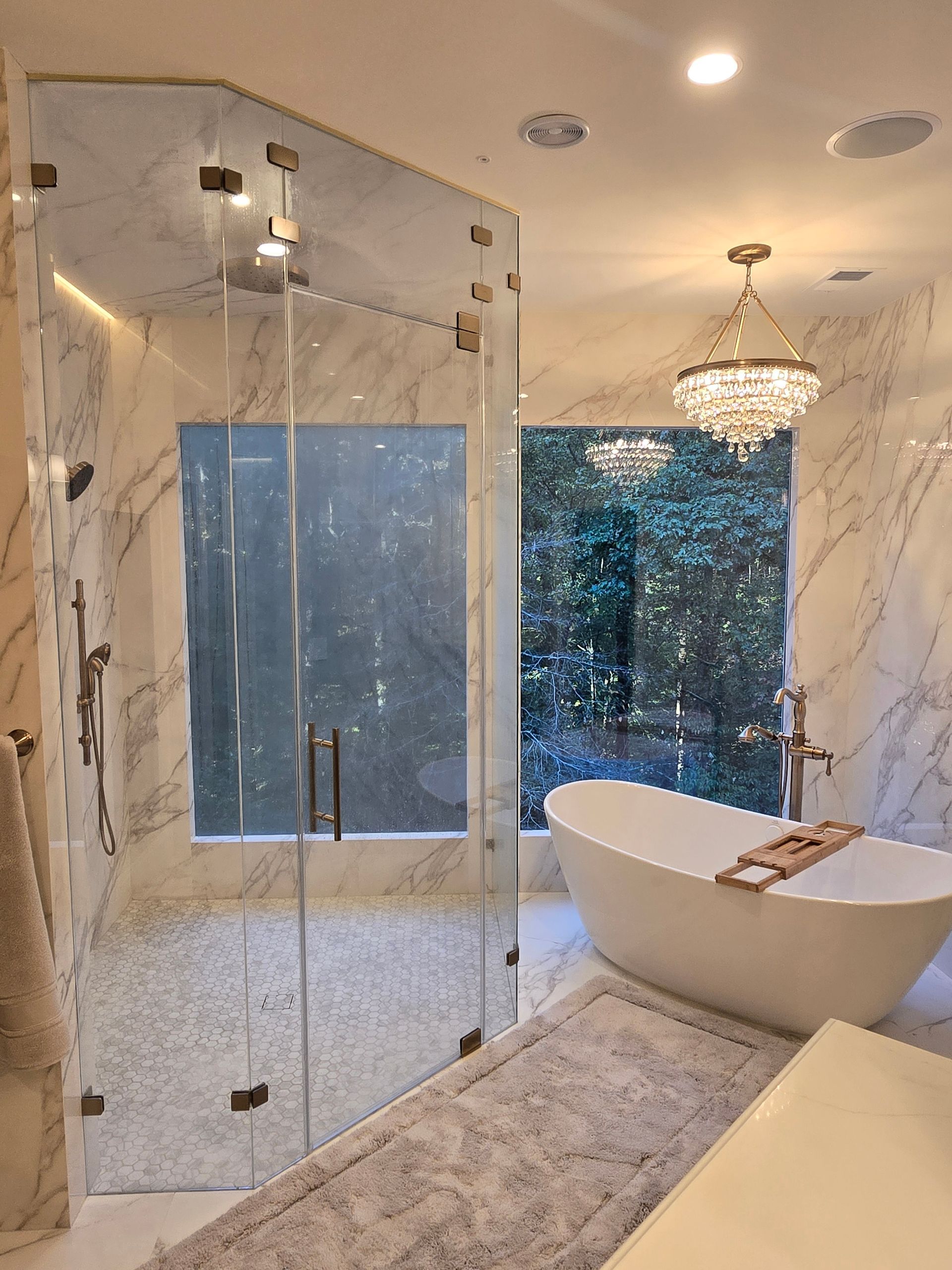Luxurious bathroom with marble walls, glass shower, and freestanding tub
