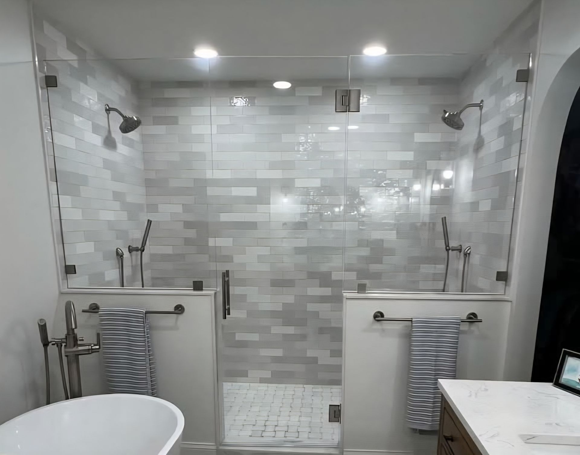 Modern bathroom with two showers, glass doors, and gray tiled walls