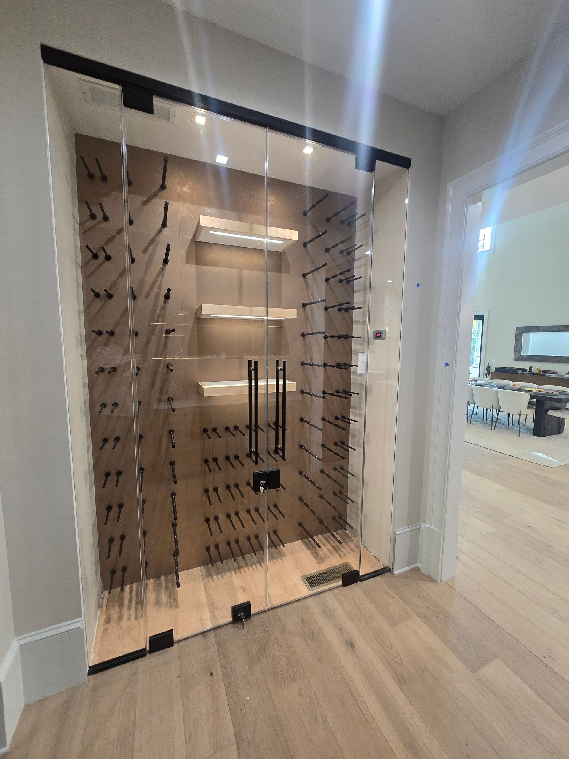 Glass-enclosed wine cellar with dark metal racks and two shelves, built into a wall