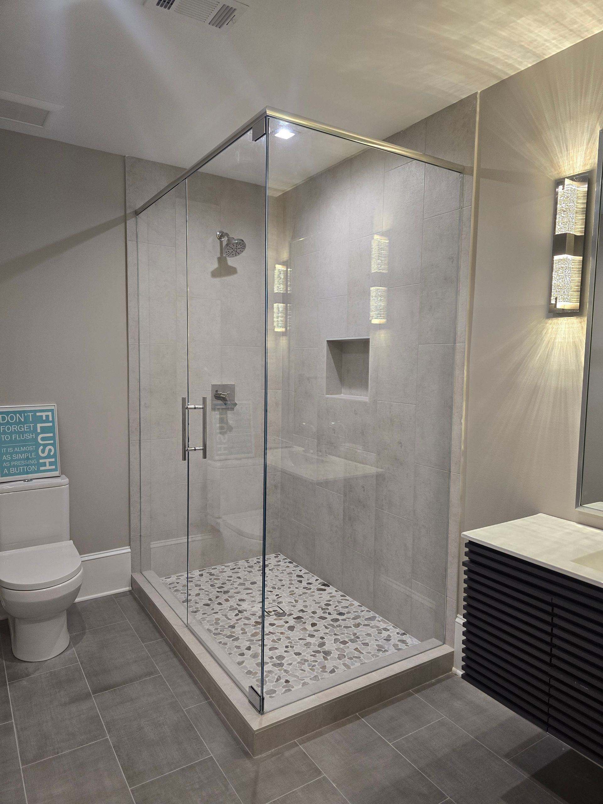 Modern bathroom with glass shower, pebble floor, and stone tile walls. Includes toilet and vanity