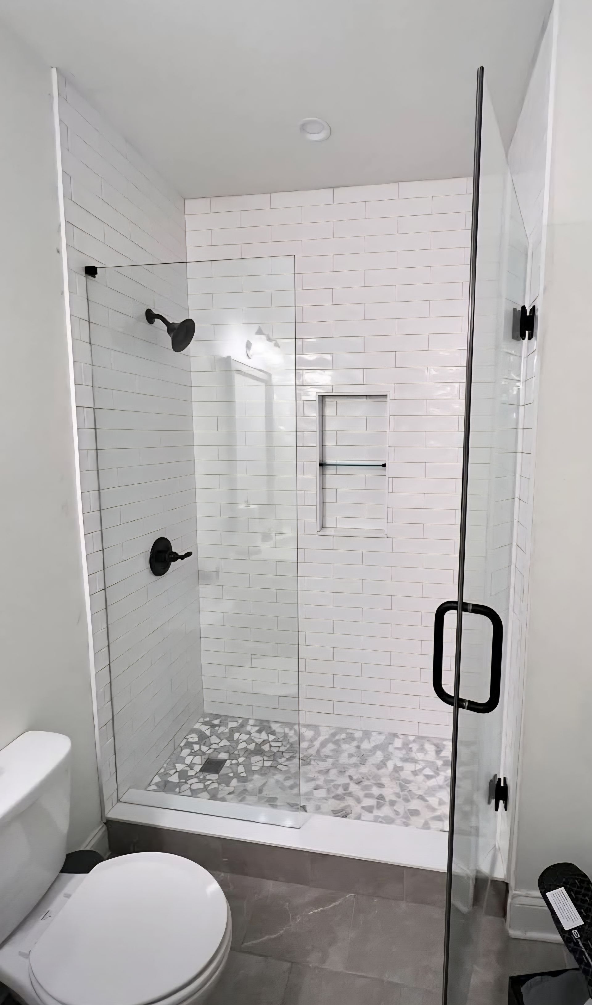 Modern bathroom shower with glass doors and white tiled walls.
