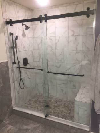 A bathroom with a sliding glass shower door and black handles.