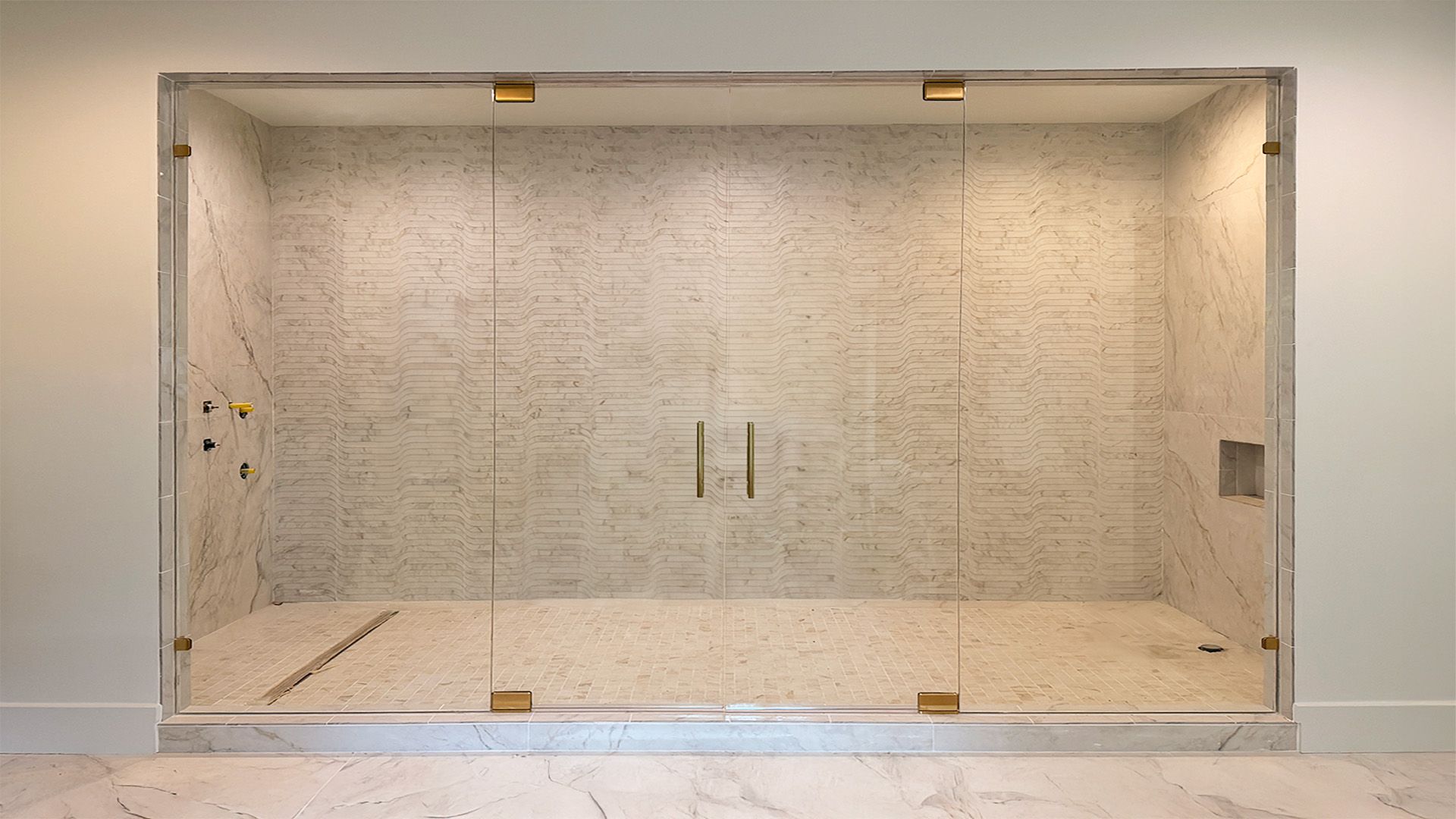 Glass shower with gold hardware, marble tile interior, double doors.