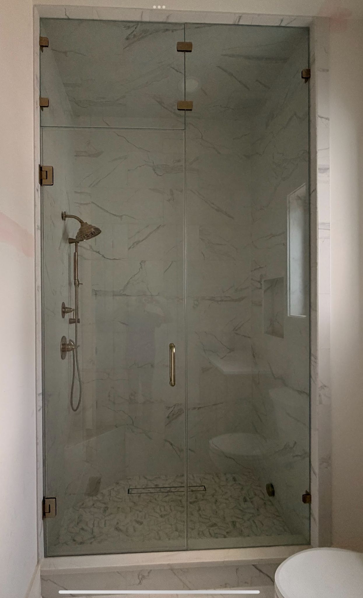 Glass shower enclosure with gold hardware, marble tile, and a pebble floor.