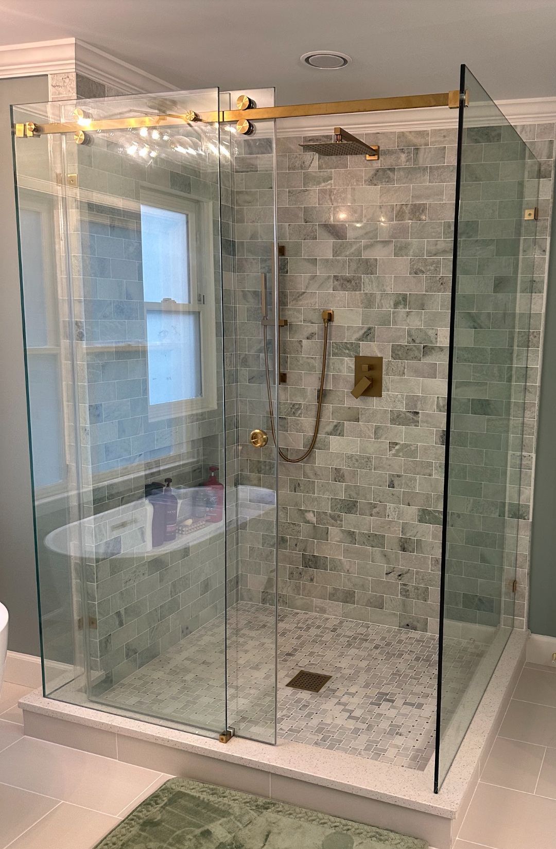 A luxurious bathroom with a glass-enclosed shower, gold fixtures, and light gray tiled walls.