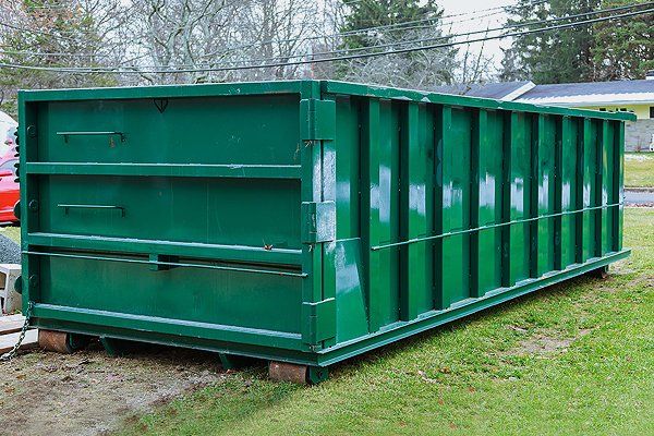 A large, rectangular green metal dumpster sitting on a patch of grass.