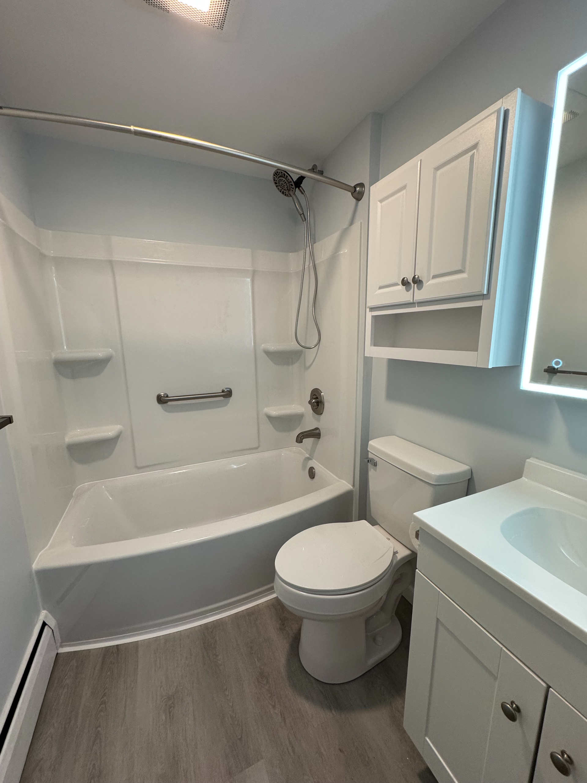 Bathroom with a white tub and toilet, vanity, and cabinet; light blue walls, gray flooring.
