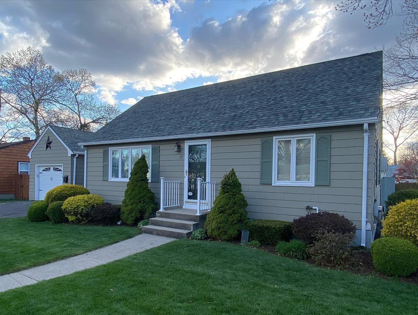 A small house with a gray roof and white shutters is sitting on top of a lush green lawn.