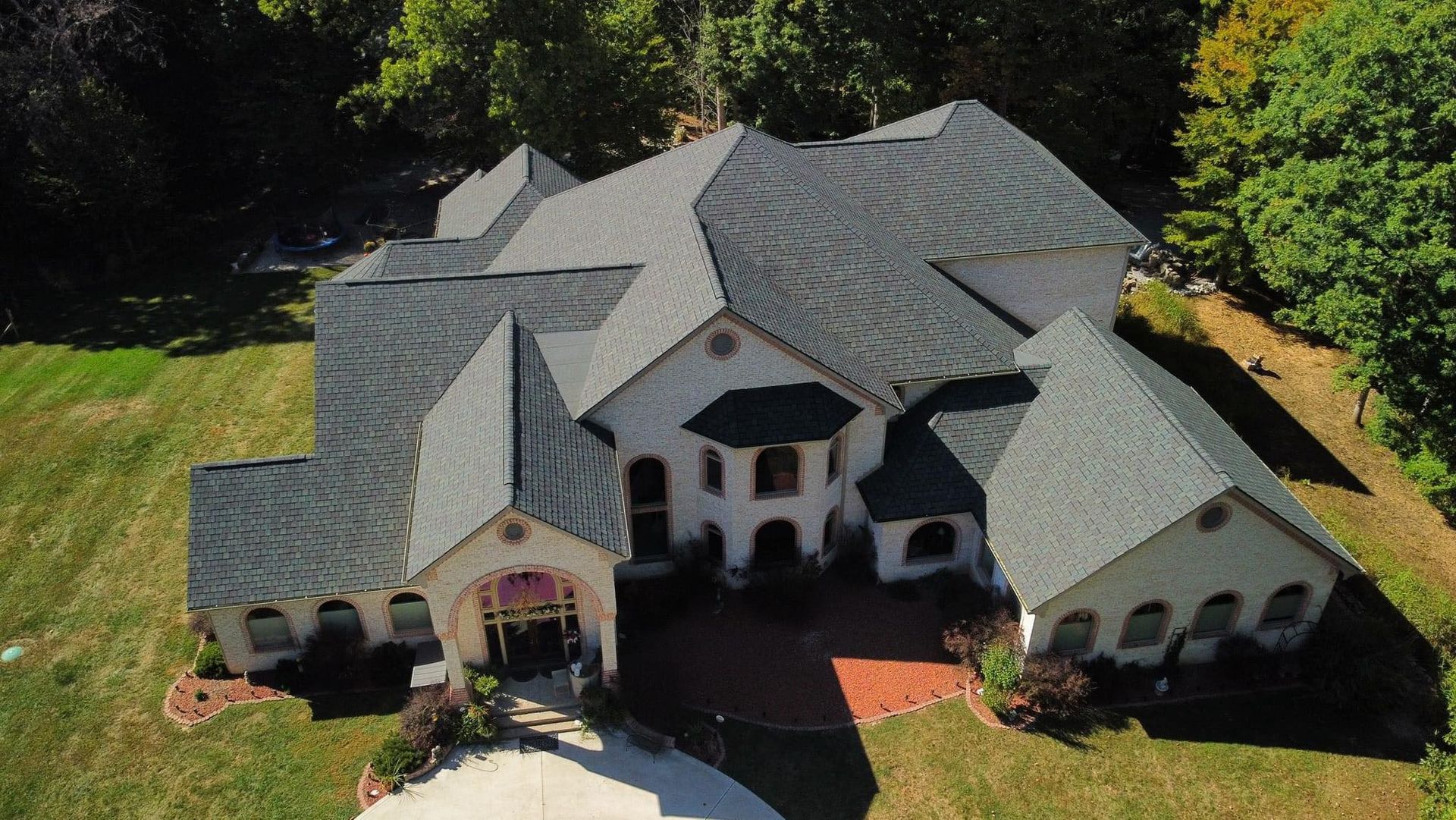 An aerial view of a large white house with a gray roof surrounded by trees.