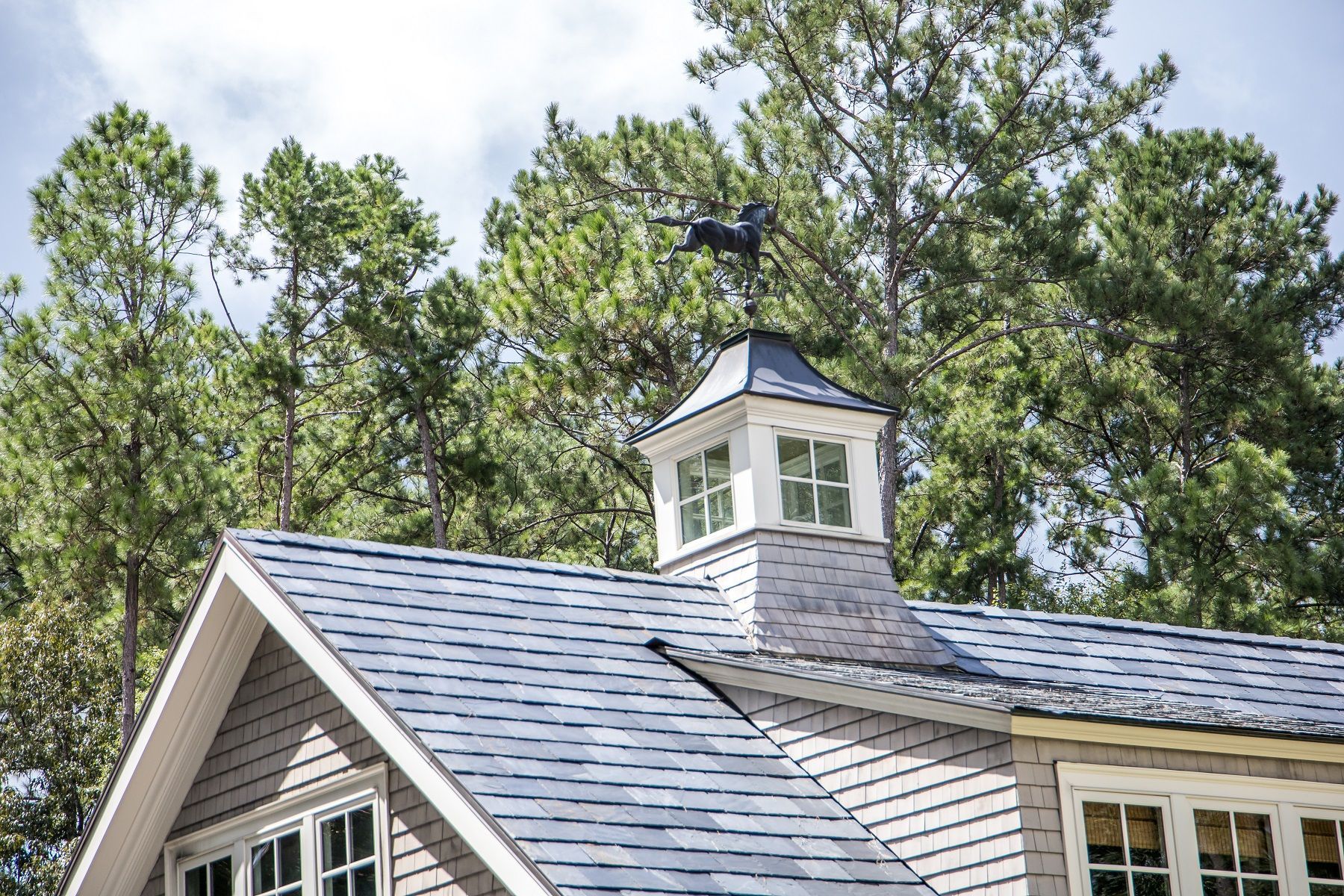 A house with a weather vane on top of it surrounded by trees.