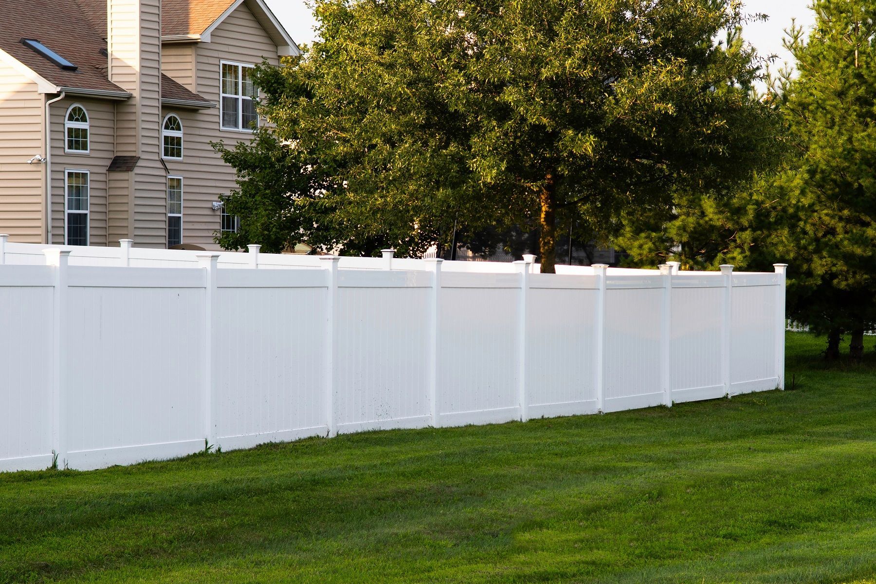 A white fence surrounds a lush green yard in front of a house.