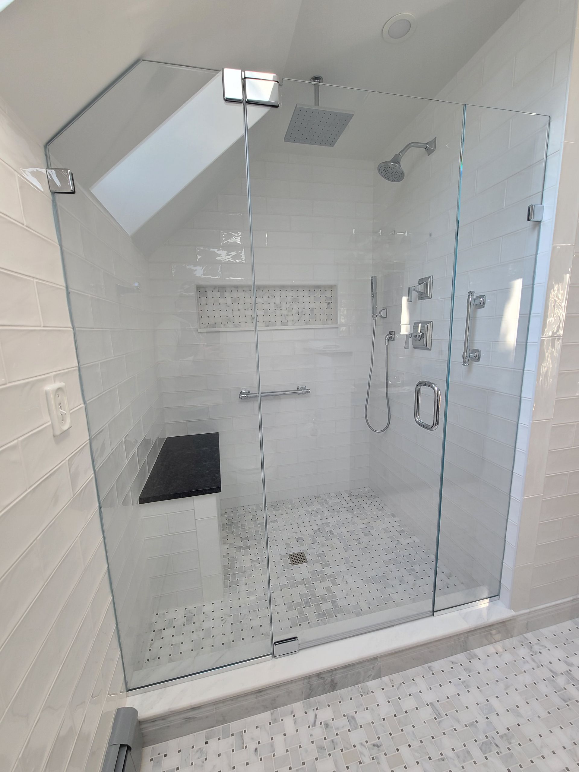 Modern white tiled shower with glass doors, built-in bench, multiple showerheads, and angled ceiling.