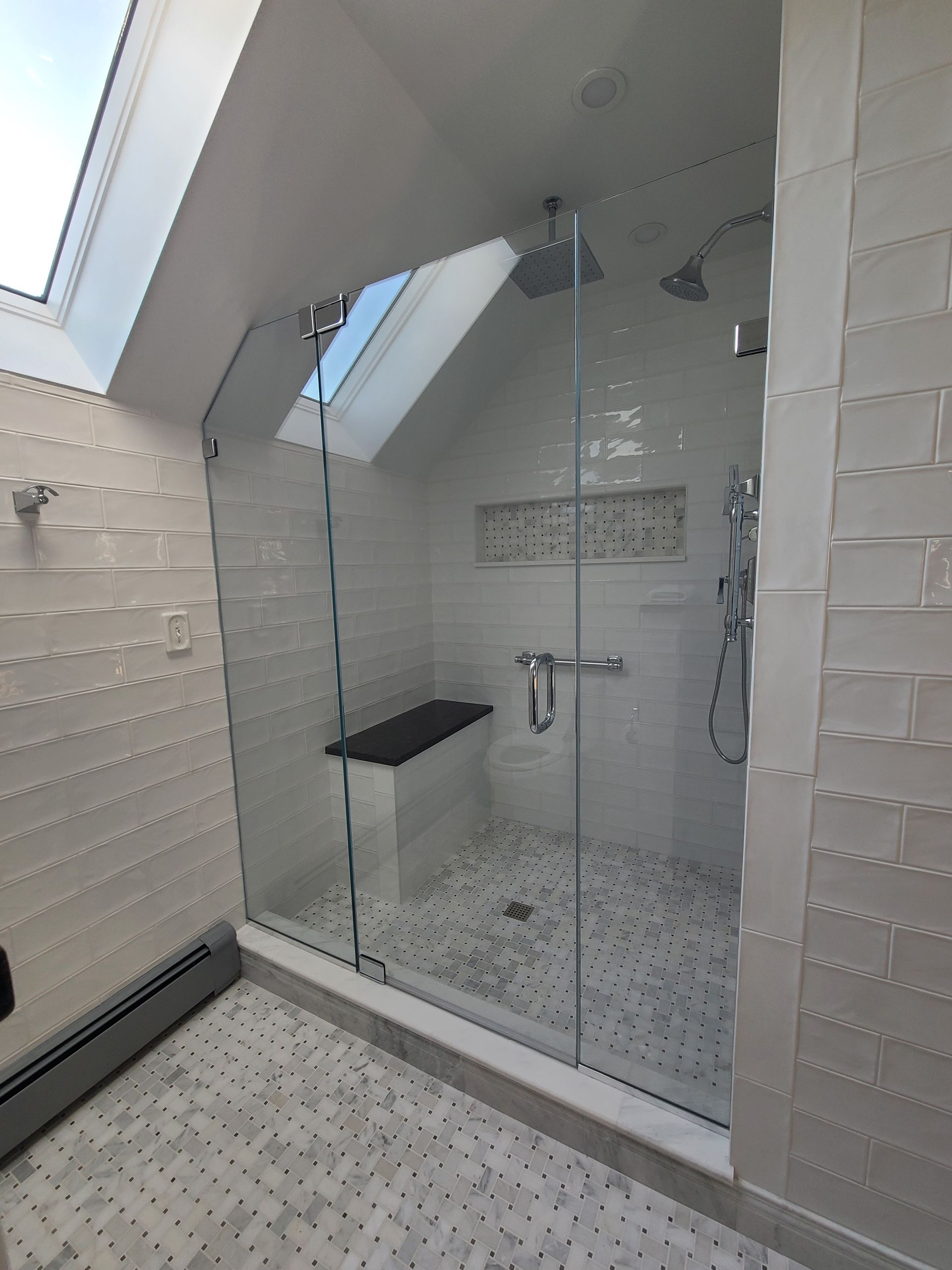 Modern shower with glass door and white tiles. Includes a built-in seat and rain showerhead.