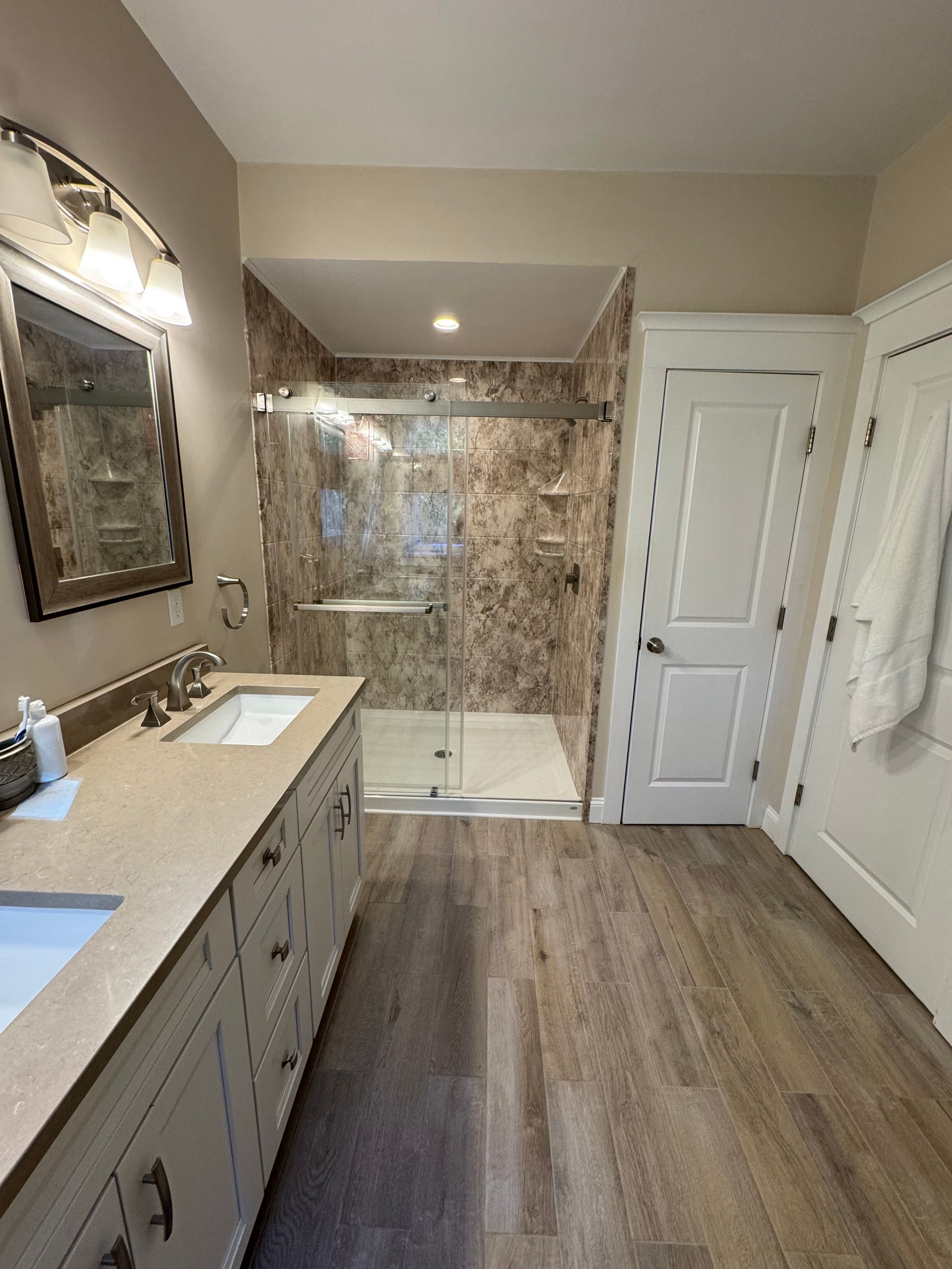 Bathroom with long vanity, shower with glass doors, and light wood flooring.