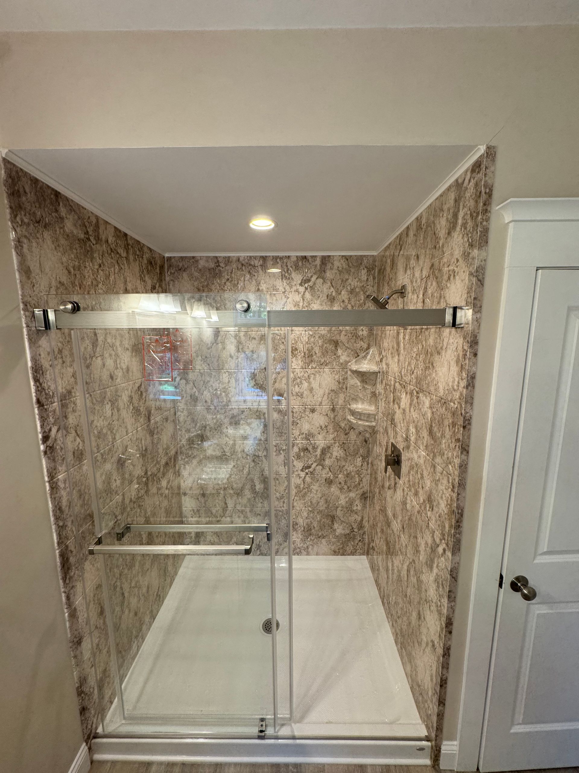 Shower stall with sliding glass doors, tan patterned walls, and white floor, in a bathroom.