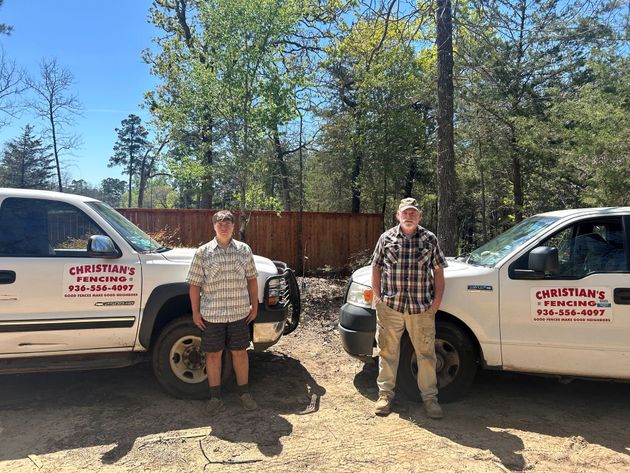 Two people standing in front of two white company trucks parked in a wooded area.