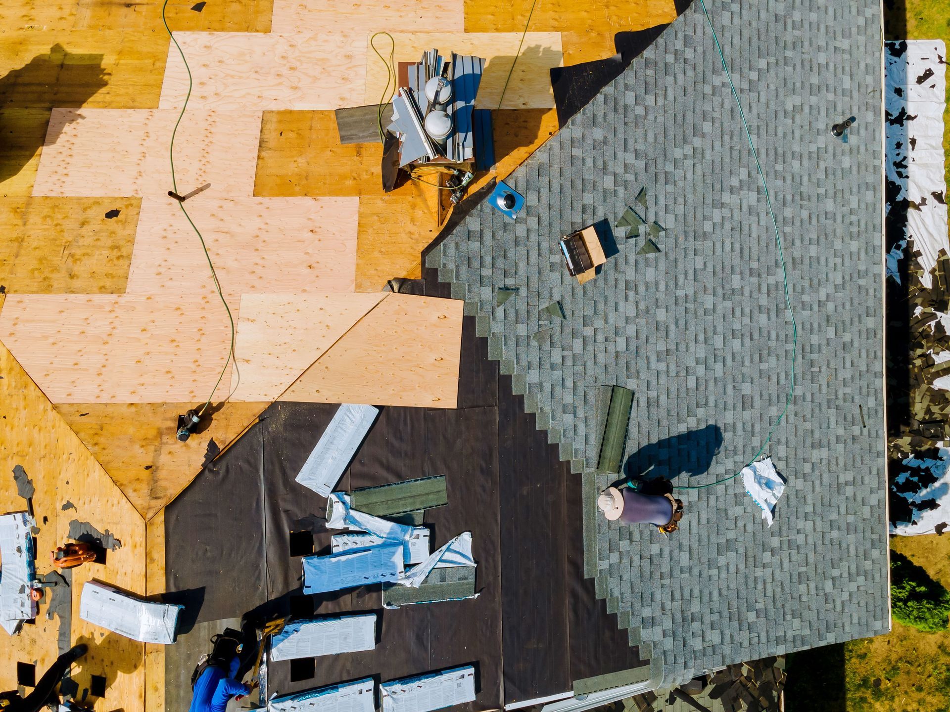 Roof being repaired; layers of shingles and underlayment visible, worker installing.