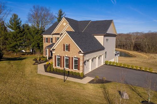 Two-story brick and siding house with a three-car garage and long driveway, set in a grassy yard.