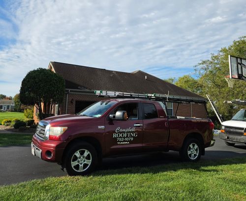 Maroon pickup truck parked on grass beside a building under a sunny sky